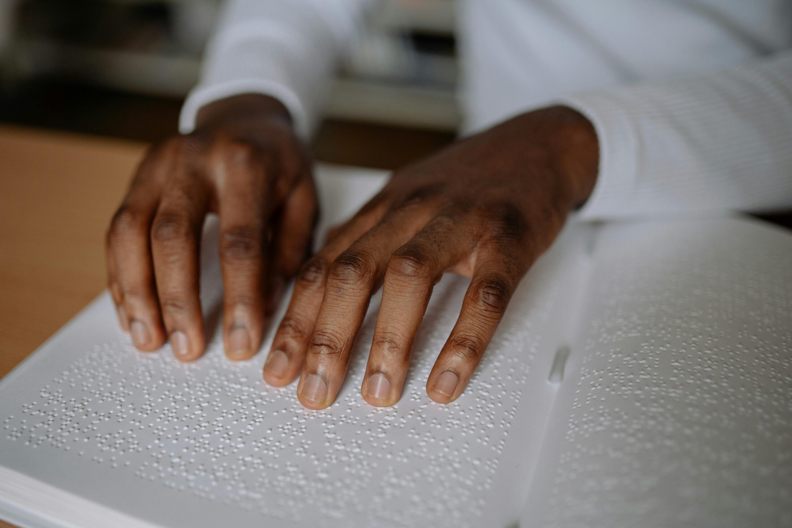 A close-up shot of hands reading a Braille book, highlighting visual impairment and accessibility.