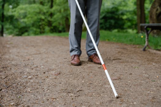 An individual with a white cane walking on a path, symbolizing independence and mobility.